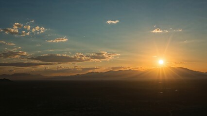 A sunset over a mountain range with clouds and a glowing sun on the horizon.