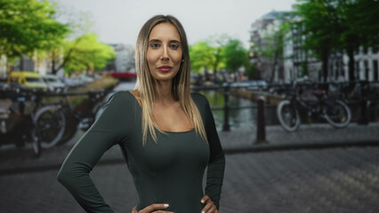 Fototapeta premium Woman with hands on hips showing shoulders at street canal in amsterdam; confidence travel exploration.
