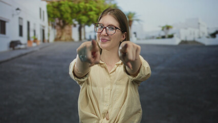 Woman wearing glasses pointing finger on sunlit empty urban street lined with white buildings;...