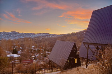 A-frame cabins on snowy hillside at sunrise, under construction, forest retreat with mountain view.