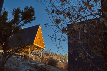 A-frame cabins on stilts in forest at sunset, minimalist autumn retreat with metal roofs and wood interiors.