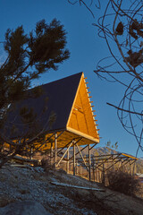 A-frame cabins on stilts in forest at sunset, minimalist autumn retreat with metal roofs and wood interiors.