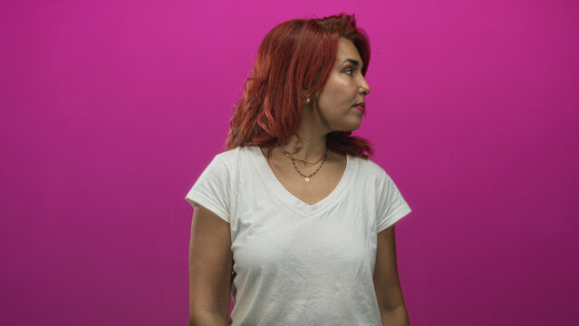 Woman face turned left, wearing white tee and necklaces, gaze averted in a studio with magenta backdrop; calm contemplation.