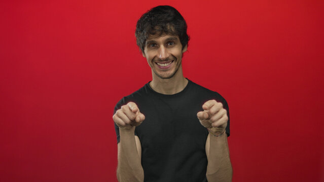 Young man creates finger heart gesture and then playfully blows kiss toward camera in red studio; affection.