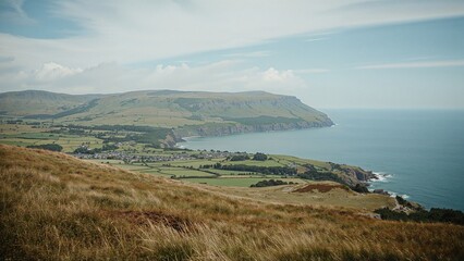 Scenic coastal landscape with cliffs and grassy fields overlooking the ocean, under a partly cloudy sky.