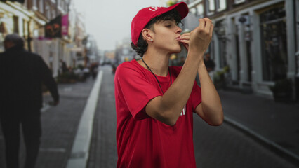 Lifeguard man in red shirt and cap blowing a whistle and raising both arms on a busy street,...