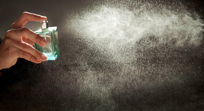 A hand holds a bottle of perfume spraying the liquid into a fine diffusion in the beautiful sunset light