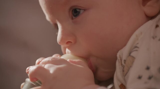 Close-up view of adorable baby drinking milk from bottle while lying comfortably in arms of her parent. Vertical format video