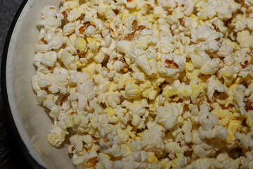 Freshly made, airy popcorn fills a white bowl in a close-up shot, ready for a movie night or a cozy evening. A generous amount of textured white and yellowish kernels creates an appetizing background.