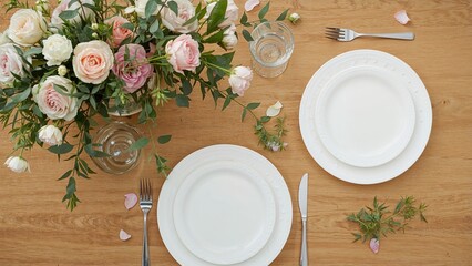 A table setting with white plates, cutlery, glasses, and a floral centerpiece on a wooden table.