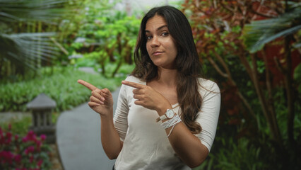 Fototapeta premium Woman points index fingers to the left on a park path with visible wristwatch and bracelets; playful curiosity.