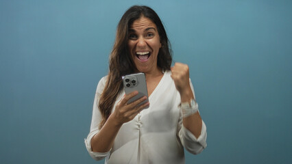 Woman holding smartphone with thumbs scrolling, looking down at screen in blue studio wearing white...