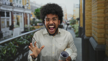 African american man with afro hair holding blueprints gesturing emphatically outdoors on a city...