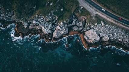 Aerial view of rocky coastline with waves crashing against rocks and a highway running along the edge.
