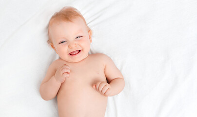 Happy ten-month-old baby lying on a white sheet with copy space