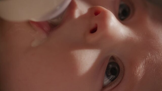 Detailed close-up view of infant sucking milk from bottle and calmly gazing upward during feeding session. Vertical format clip