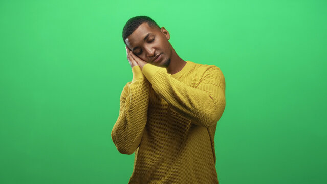 Man in yellow sweater rests head on hands and closes eyes in a sleep gesture against green screen in studio, then claps and returns to neutral pose; calm. - Powered by Adobe