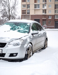 A car with a shattered windshield sits in a snow-covered parking lot after a winter collision.