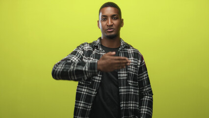 Man covers mouth with hand in studio against lime green backdrop, wearing a plaid flannel shirt and t shirt; playful confidence.