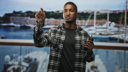Man holding electric screwdriver points finger toward camera on balcony of building, right hand gripping tool and thumb visible; skill confidence.