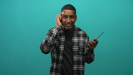 Man holding screwdriver in right hand, hand to ear listening gesture, wearing plaid flannel shirt in studio; curiosity problem solving focus.