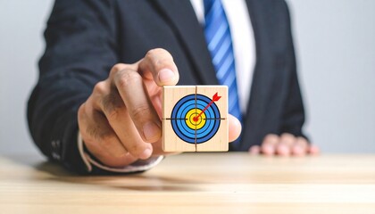 Businessperson holding wooden block with target and arrow symbol at table, emphasizing goal achievement.