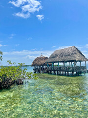 Fototapeta premium Thatched hut on wooden stilts over clear Caribbean waters near Bocas del Toro, Panama. Cloudy tropical sky