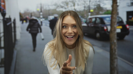 Obraz premium Smiling young woman points excitedly on a busy city street, blending with urban elements including cars and trees, capturing a moment of joyful interaction in public.