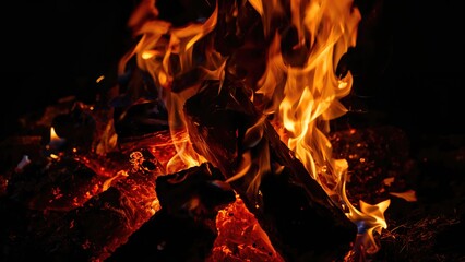 Fototapeta premium Flickering flames on burning logs with glowing embers and fire flames. Fireplace, heat, and warmth. The concept of fire and combustion.