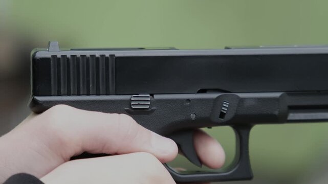 A hand reloads a pistol or cocks the pistol and fires a shot, a close-up of the trigger