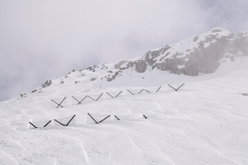 Snow-covered alpine rocks rise from a foggy winter slope, creating a dramatic and atmospheric mountain scene. Rugged terrain, soft light, and cold high-altitude conditions.