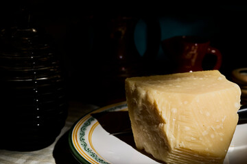 Parmesan cheese. A piece of Parmesan cheese and a jar of honey on a dimly lit table.