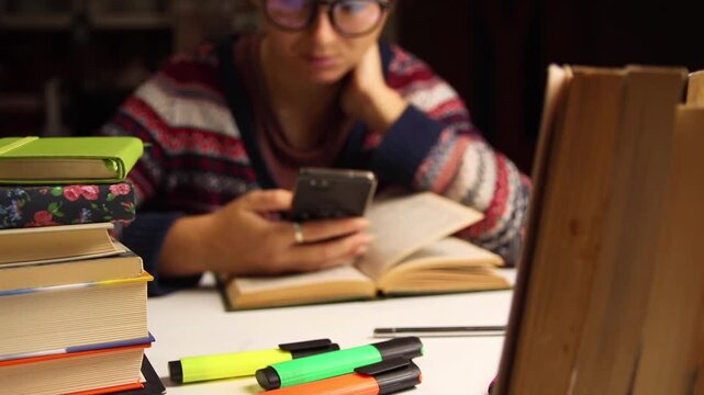 Stressed student in sweater holding head while looking at phone, surrounded by books and notes, exam pressure mood