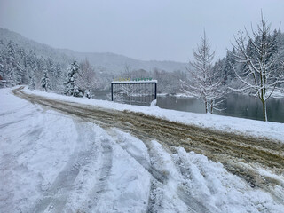 Obraz premium Snowy Winter Landscape by a Lake with Tire Tracks on a Dirty Road