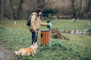 Person with a dog uses a waste disposal station in a park on a cloudy day