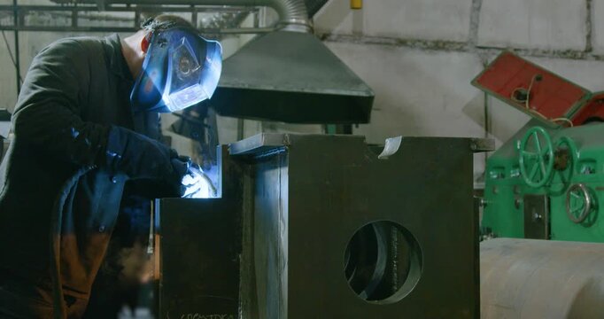 A worker welds metal in a protective helmet. Heavy industry and metallurgy. Professional at work. Industrial electrogas welding. 25 fps 6k footage.