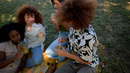 Happy multiethnic friends laughing and clinking cups together while enjoying a picnic on a sunny day in the park, celebrating their friendship and enjoying refreshing drinks outdoors