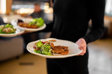Waiter serving plated breaded cutlet dish with salad at a restaurant.