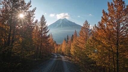 Autumn landscape with a dirt road leading towards a mountain, surrounded by colorful trees and sunlight shining through the forest.