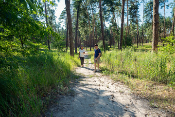 Fototapeta premium Couple hiking through a sunny pine forest on a dirt path, enjoying nature and outdoor activity on a beautiful day.