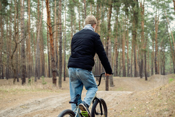 Fototapeta premium Young person rides BMX bike on a dirt trail in a pine forest, embodying outdoor adventure, youthful energy, and an active lifestyle.