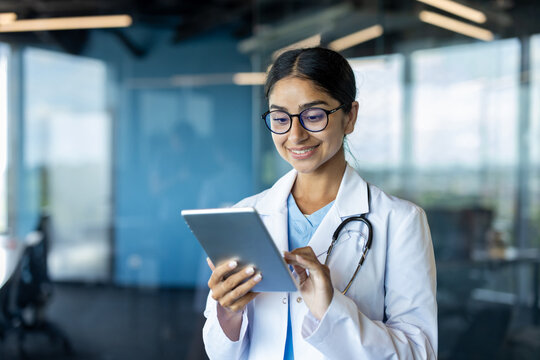 Smiling Indian female doctor standing in hospital room and using tablet