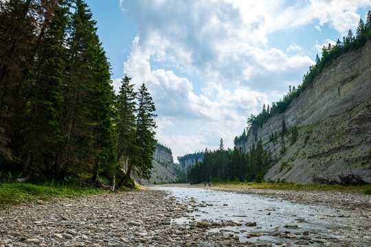 Steep Canyon, Stone Cliffs, Shallow River, Fallen Boulders, and Boreal Forest Under a Blue Sky near to Vaureal Waterfall on a Sunny Day in Anticosti, Quebec, Canda