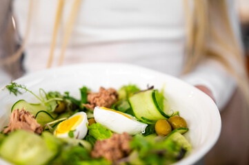 Fresh, healthy tuna salad with cucumber ribbons, boiled eggs, olives, and leafy greens in a white bowl