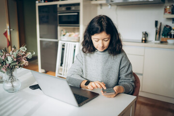 Young woman engaged in work while using smartphone at home kitchen table in the morning