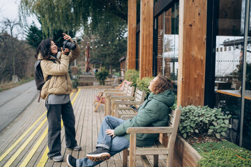 Female photographer capturing portrait of relaxed man sitting on bench outside modern wooden...