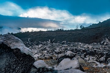 Rugged volcanic landscape of rocks and ash beneath a dramatic cloudy sky at Poás Volcano