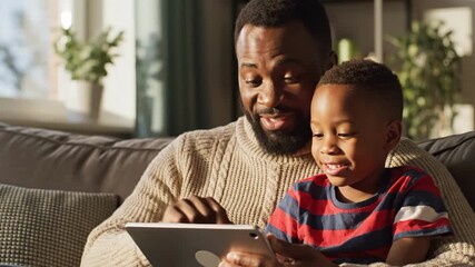 Happy african american father and young son bonding while looking at a tablet device together on a couch at home - Powered by Adobe