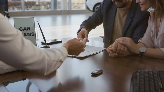 Close up shot of unrecognizable car salesman handing contract to couple of clients while sitting at desk and signing contract buying new car, copy space