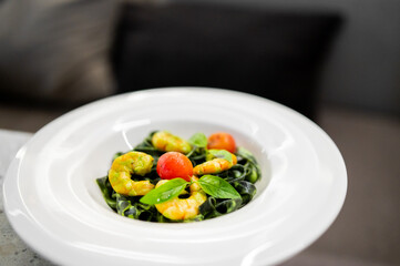 Vibrant spinach tagliatelle with succulent shrimp, fresh cherry tomatoes, and basil on a white plate.